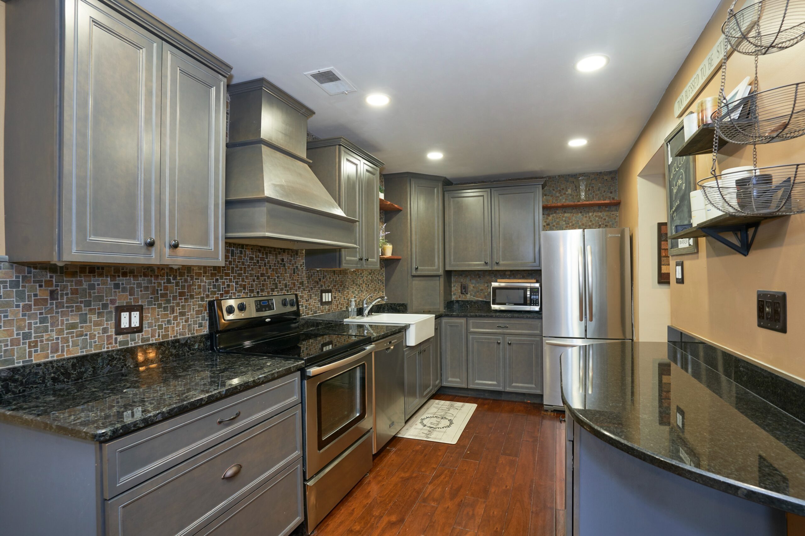 Professional interior photo of 10675 Spring Oak Ct - showing the kitchen with updated grey cabinets, dark granite countertops and stainless appliances with custom range hood