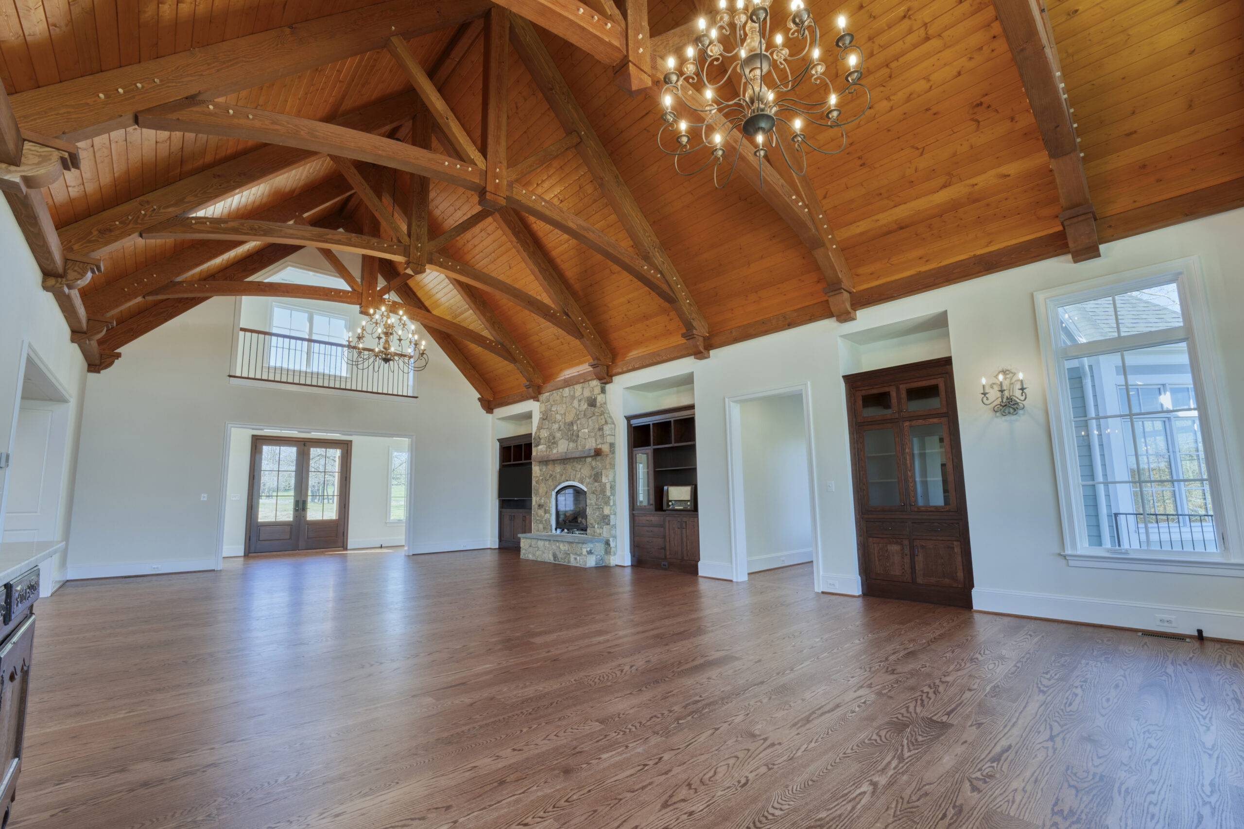 Professional interior photo of custom build new home by Black Oak Construction - showing the great room with hardwood floors, vaulted wooden ceiling with wooden trusses, stone fireplace and built-in cabinets on either side