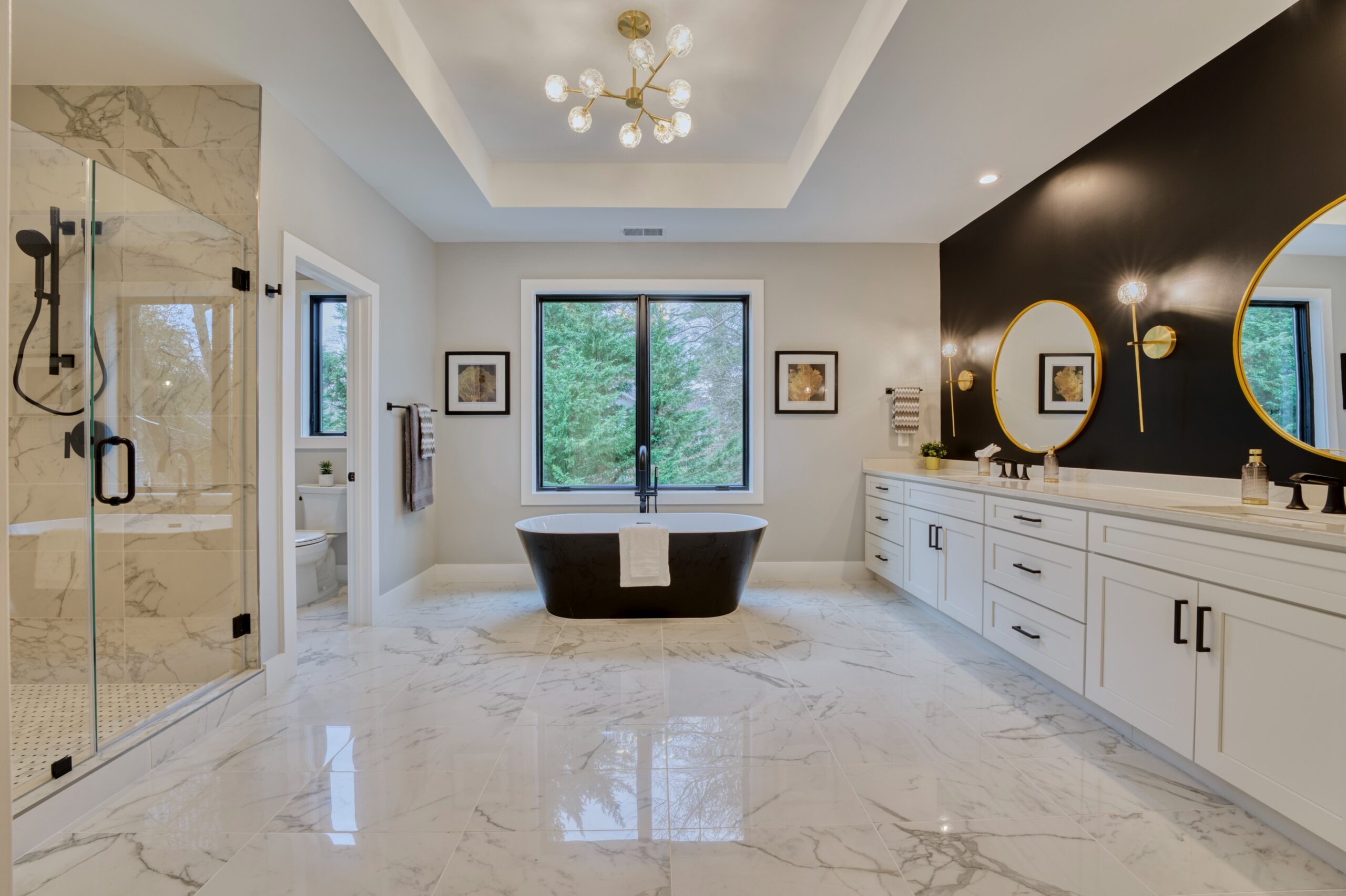 Professional interior photo of new construction home at 3400 N Ohio St - showing the primary bathroom with marble floors, shower, deep soaking tub, tray ceiling and black and gold accents