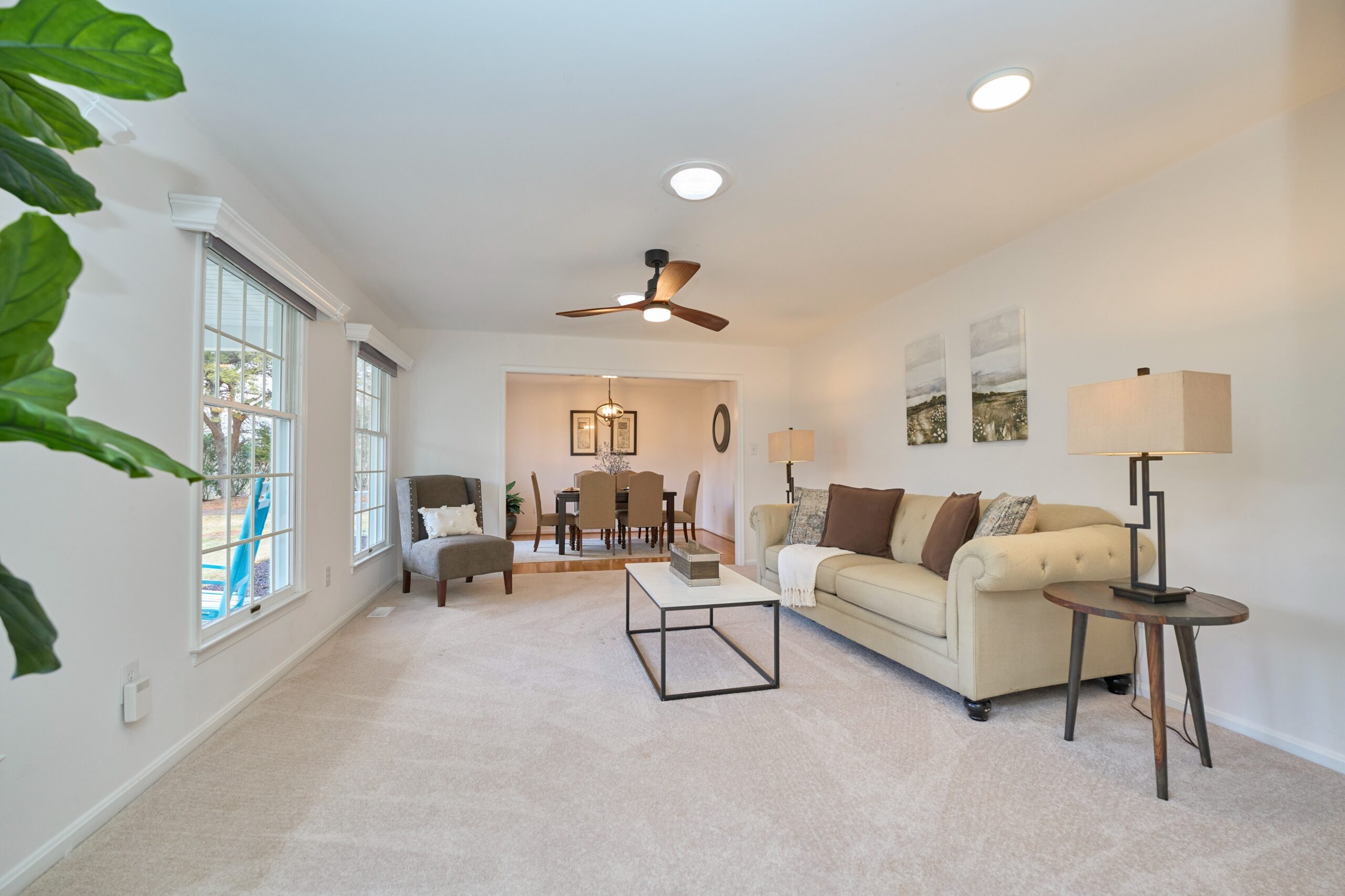 Professional interior photo of 3103 Indian Run Rd - showing the front sitting room with cool ceiling fan, freshly painted white walls, and plush carpets with large windows and natural light as well as solar tubes