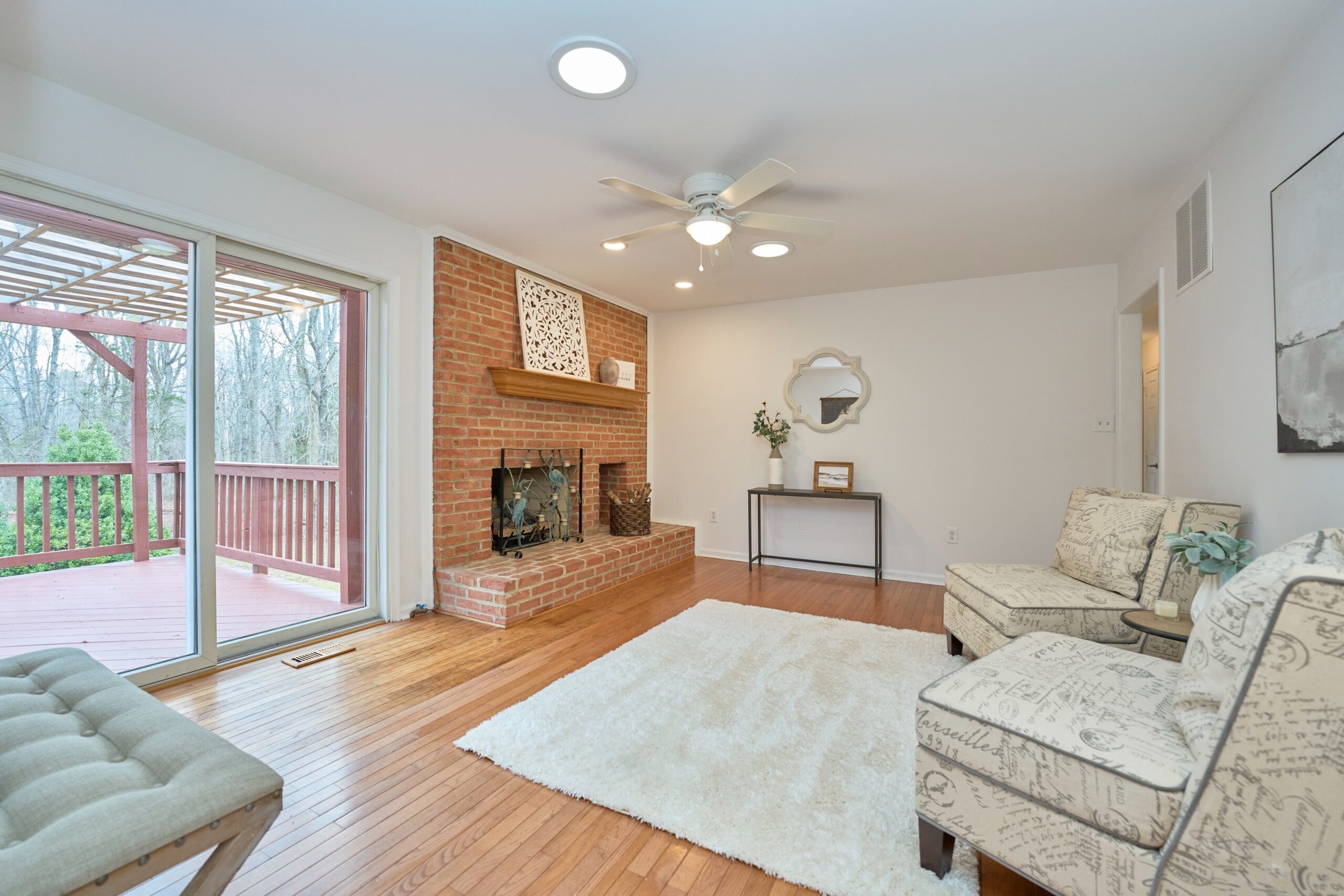 Professional interior photo of 3103 Indian Run Rd - showing the upstairs living room with brick fireplace, hardwood floors, and sliding glass doors to the rear deck off the main level