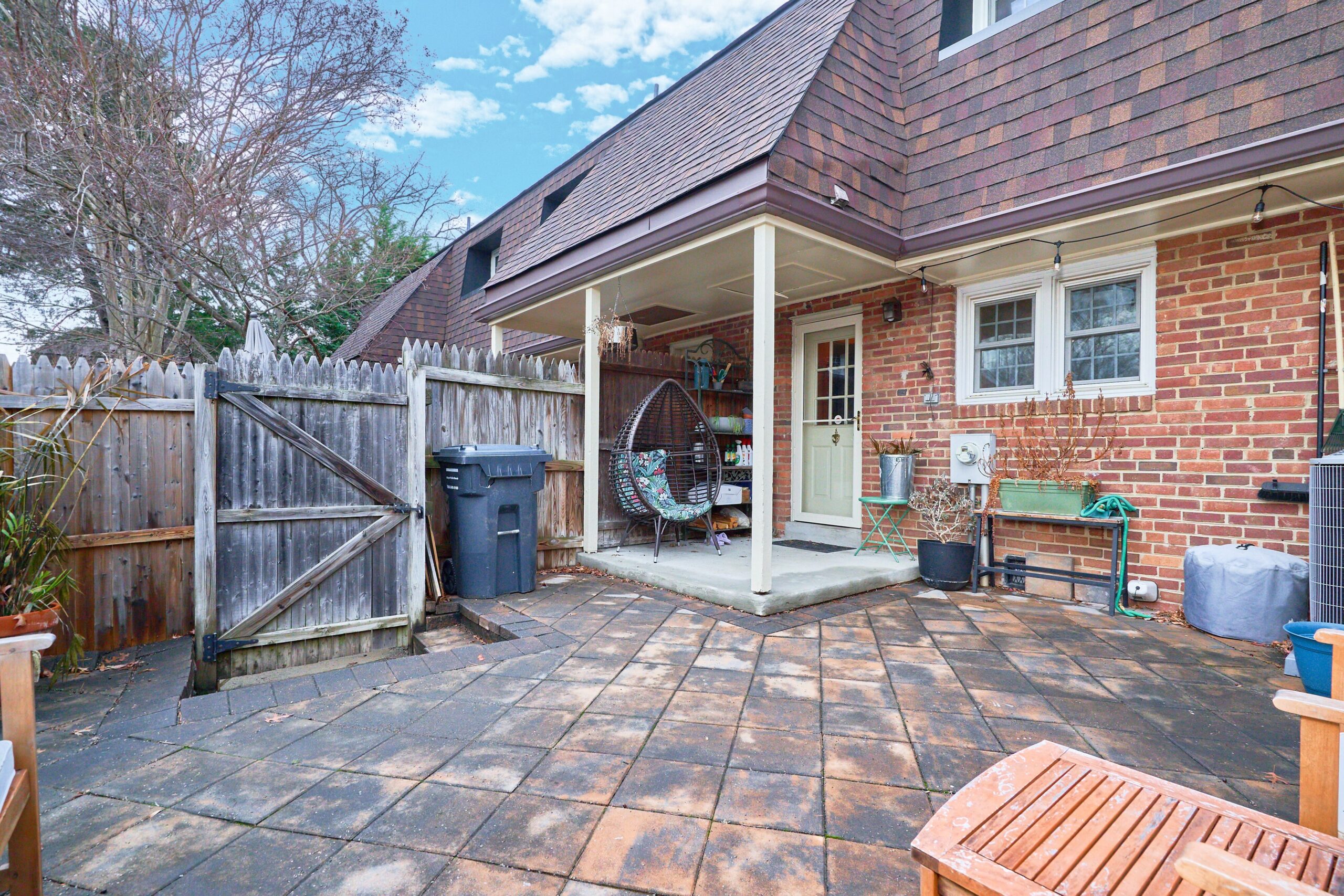 Professional exterior photo of 415 James Ct in Falls Church City - showing the rear fenced patio with covered back porch, brick exterior, and wooden gate to exit.