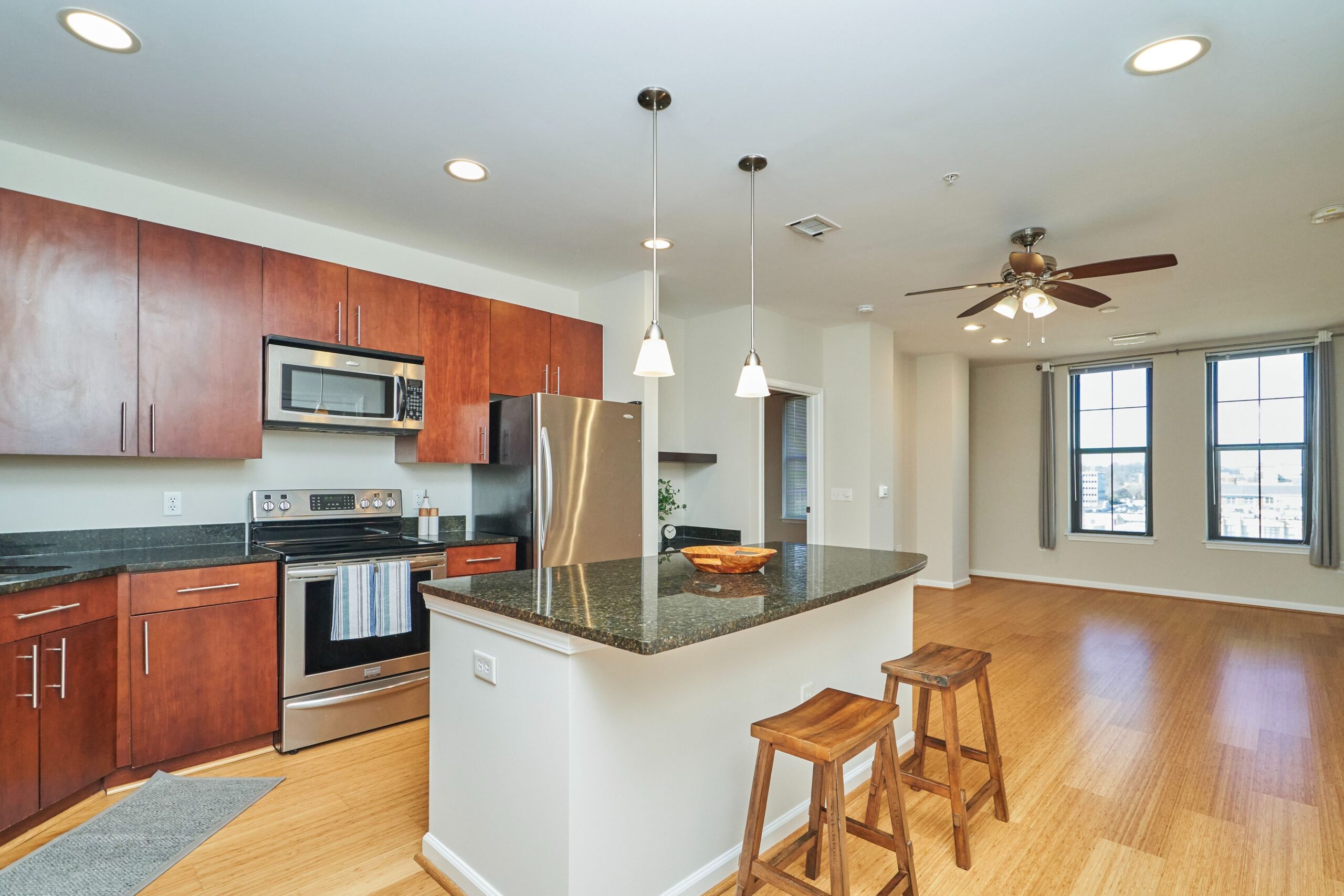 Professional interior photo of 444 W Broad St Unit 631 - showing the open kitchen and living area with granite island, hardwood floors, ceiling fan