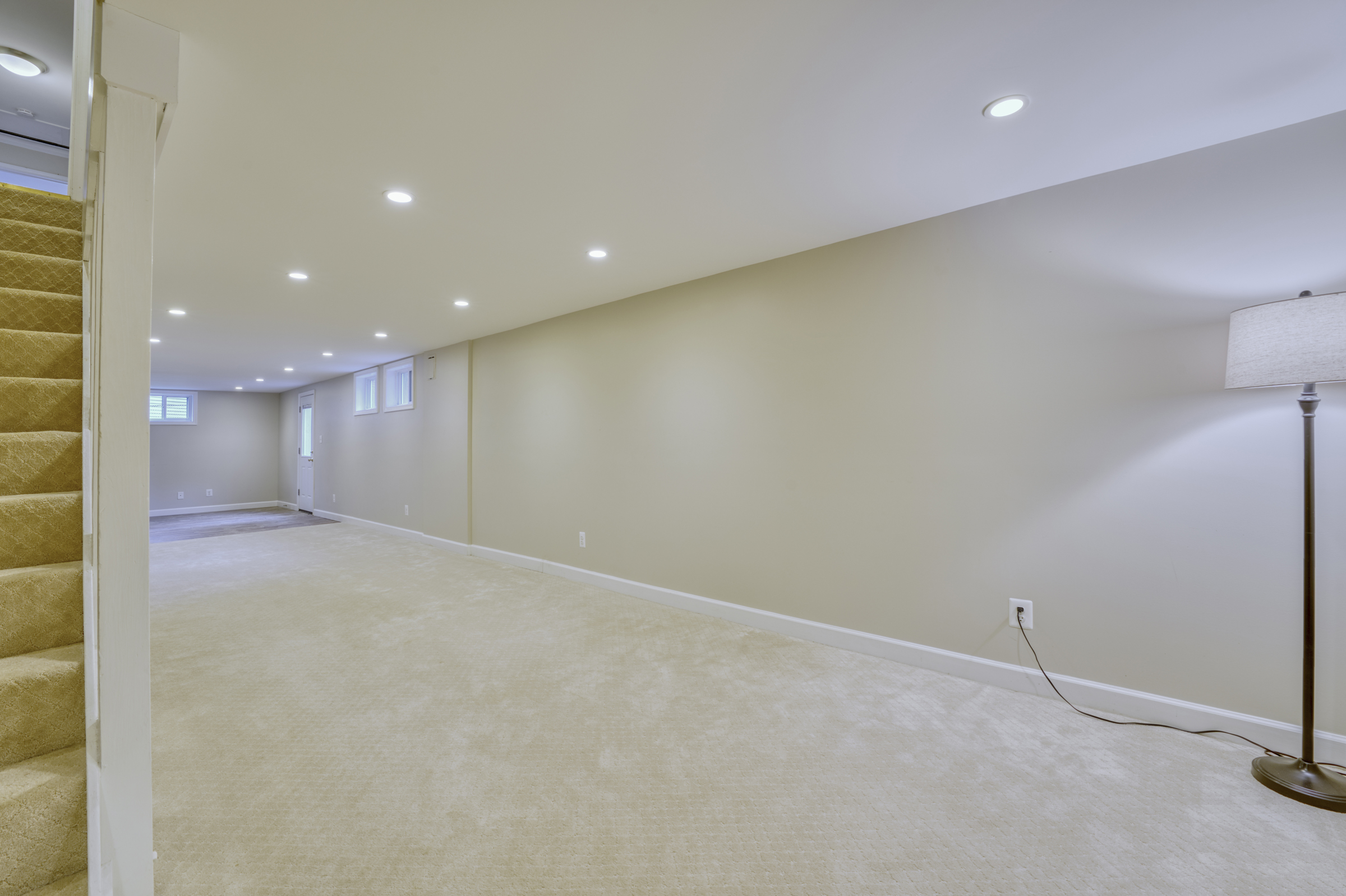 Professional interior photo of 2624 Depaul Dr in Vienna, VA - showing the main area in the fully finished basement with beige carpeting and the staircase to the upper level in the front left
