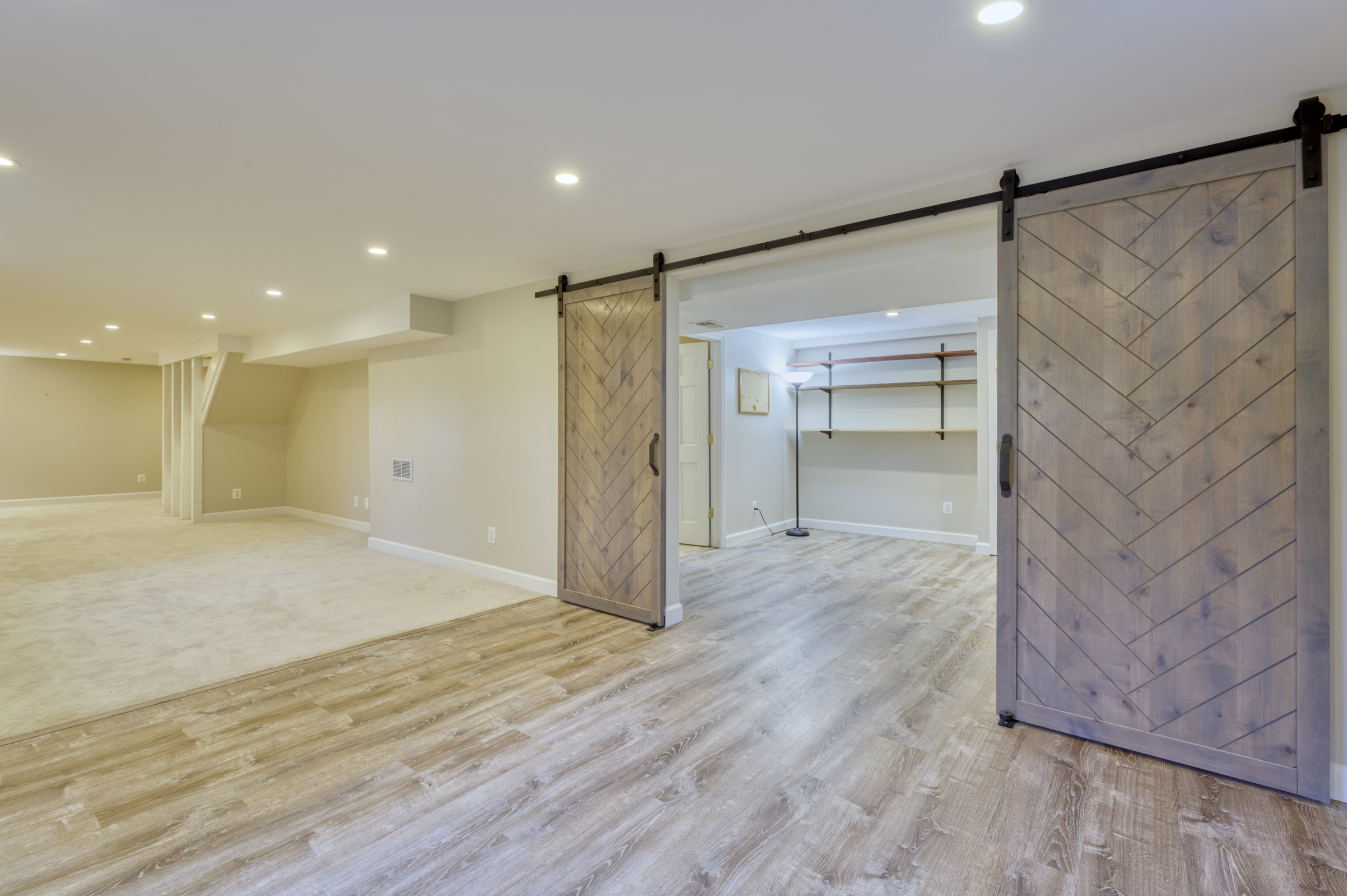 Professional interior photo of 2624 Depaul Dr in Vienna, VA - showing the main area in the fully finished basement with beige carpeting and looking through barn doors to the game room